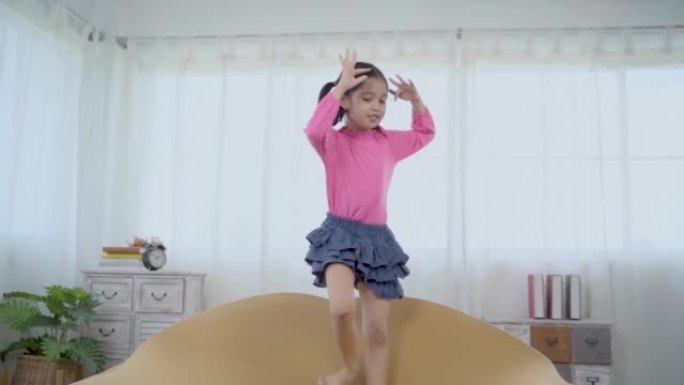 慢动作，亚洲可爱的小女孩跳舞，快乐地跳上沙发。有趣的孩子跳舞，独自在家玩耍，享受音乐创造风格的舞蹈，