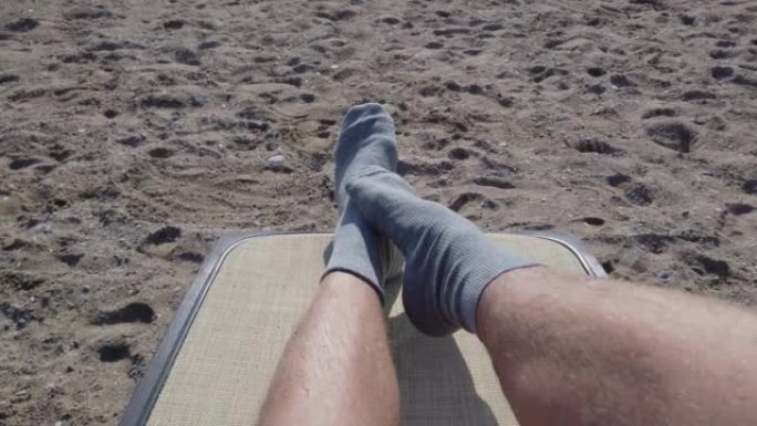 跳舞，扭动袜子中的男性腿和脚趾。一个躺在躺椅上，在海滩上晒日光浴的人的观点。做奇怪奇怪有趣事情的概念