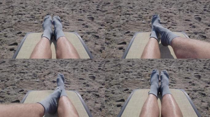 跳舞，扭动袜子中的男性腿和脚趾。一个躺在躺椅上，在海滩上晒日光浴的人的观点。做奇怪奇怪有趣事情的概念