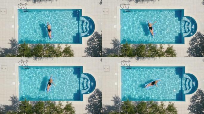 游泳池上的4k镜头，穿着黑色泳衣的放松女人，草帽漂浮在橄榄树下蓝色涟漪水面的充气床垫上。假期，娱乐概