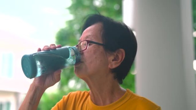 亚洲老年妇女在家晨练后喝水。