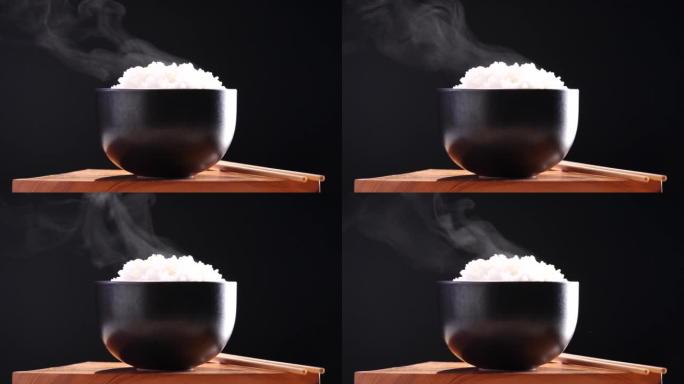 日本米饭，米饭。用黑色背景上的筷子在黑色碗中关闭自然蒸煮的日本白米饭，柔和对焦。健康食品概念。
