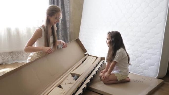 年轻的单身母亲带着女儿看着孩子们卧室里未来床的盒子里的东西。家具的内部结构。单身母亲的概念。家庭活动