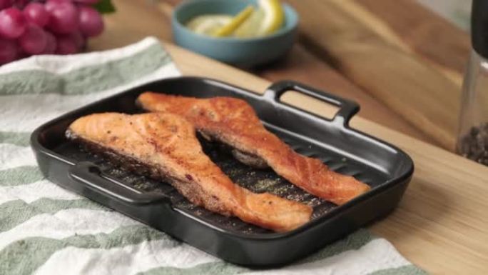 慢动作4k视频，烤烤鲑鱼片在黑色盘子上撒上欧芹草本和黑胡椒片。鲑鱼健康饮食和高蛋白质饮食