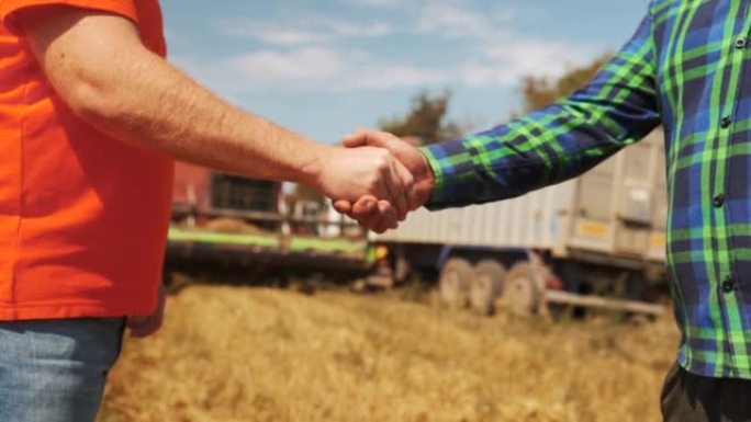 达成协议后，农民和农艺师站在麦田里握手。农业商业合同概念。联合收割机司机和牧场主就收割季节进行谈判。