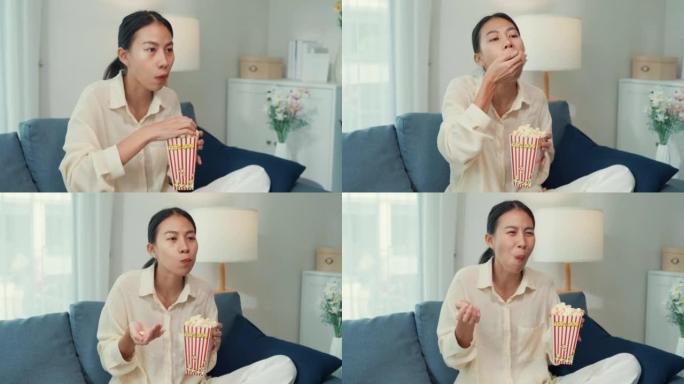 年轻的亚洲女孩在沙发上吃爆米花有趣的笑声观看喜剧频道电影或情景喜剧在电视上播放在线视频点播，在家点播