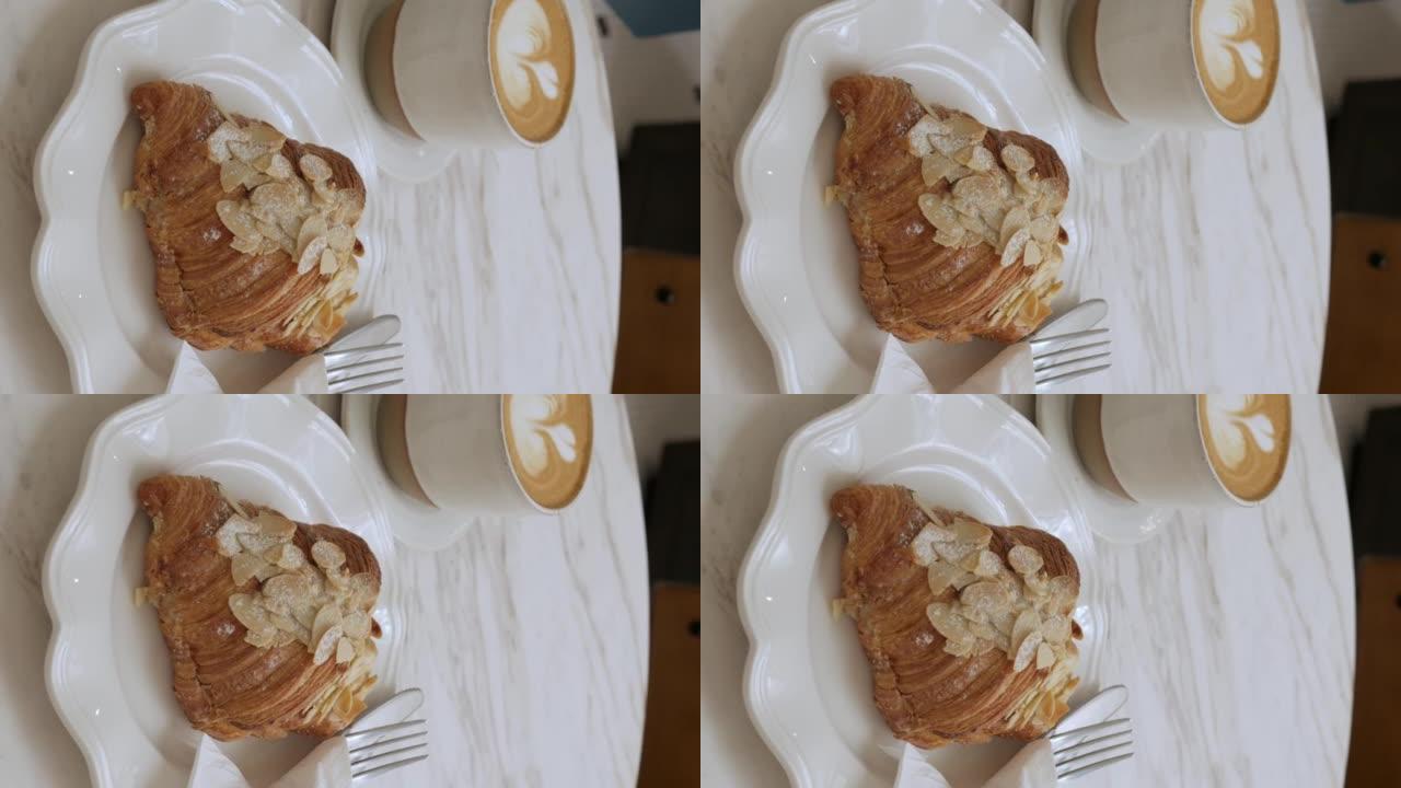 咖啡馆白色大理石桌子上盘子里杏仁羊角面包的垂直视频视图，盘子里有叉子和刀具，面包店烤糕点