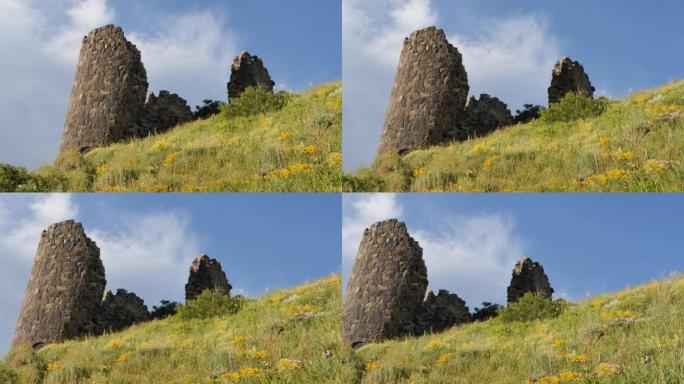 在一片绿色的田野和蓝天的背景下，一座古老的石头堡垒的防御墙和塔楼的碎片。今天保存的历史古迹