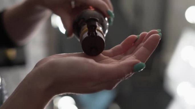 背景上的小瓶子里的液体倒入一个女孩的手中，特写镜头。女人从小瓶里用手倒油。