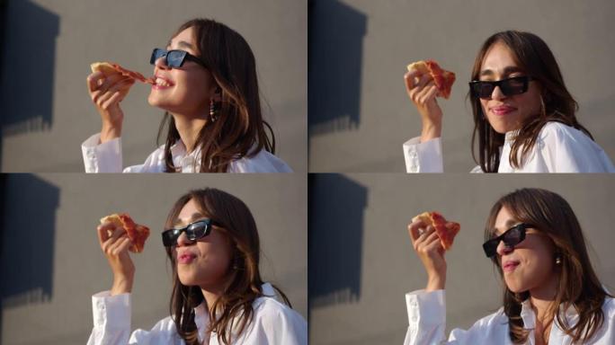 戴墨镜的女孩正在吃披萨。女孩咬披萨，微笑和跳舞