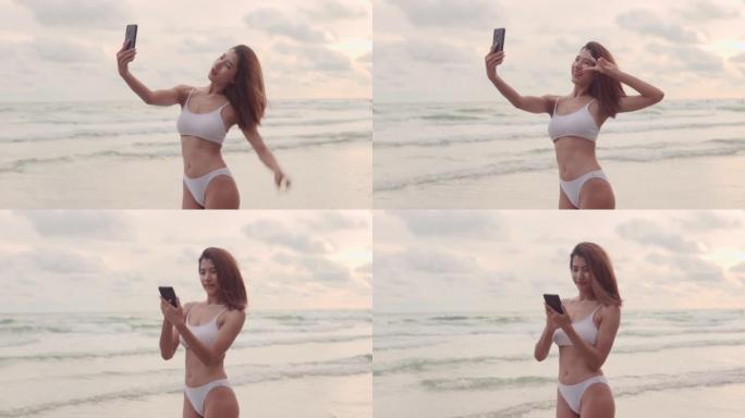 年轻的亚洲妇女使用智能手机，度假时在海滩上散步，使用电话进行交流。
