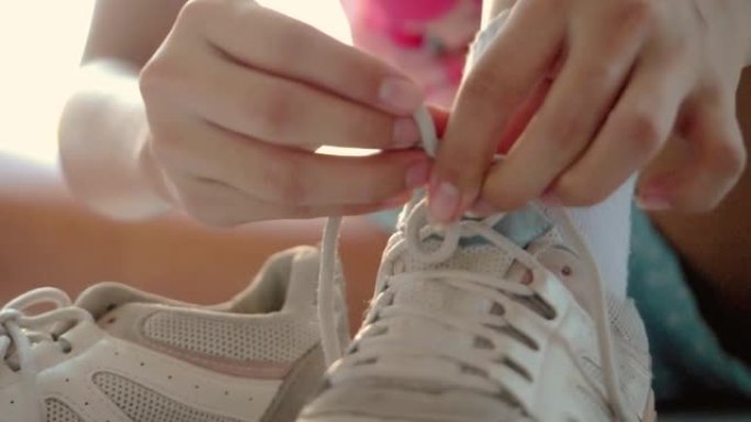 女孩的手穿着运动鞋和系鞋带，然后在户外玩滑板，生活方式概念。