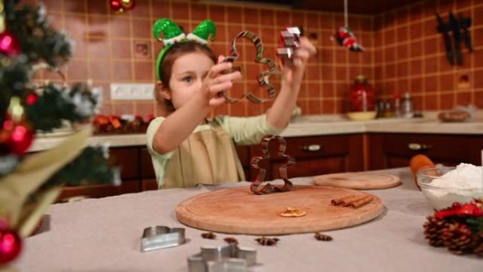 看圣诞树和改变焦点一个可爱的小女孩在厨房里玩姜饼切刀