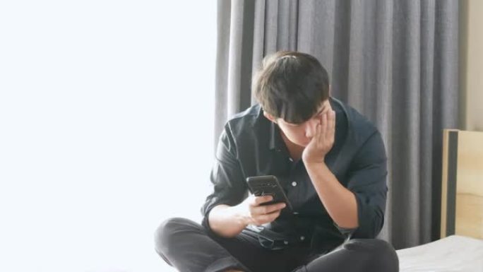 亚洲男子看到手机发来的意外信息后感到失望和沮丧，悲伤和失望的情绪，坐在床上压力很大，被解雇了，心碎了