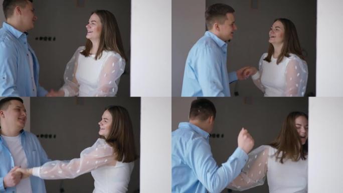 年轻兴奋的高加索夫妇在新的平面舞蹈微笑中玩耍。快乐快乐的千禧一代男女在室内购买公寓。移动和关系。