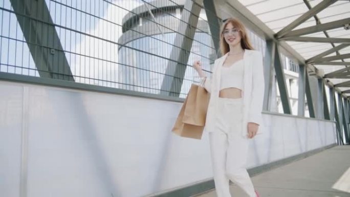 穿着白色西装的性感微笑女人带着购物袋在城市街道上行走。Steadicam慢动作稳定射击