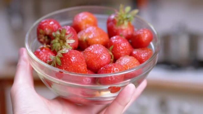 双手女性拿着满满的玻璃碗红色的草莓在阳光下。特写