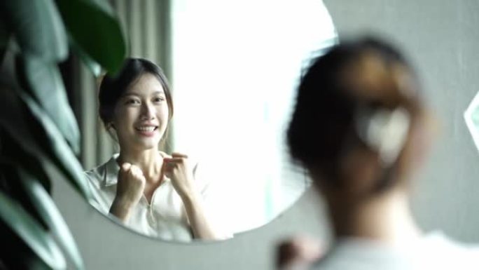 一位年轻的亚洲妇女通过镜子与自己交谈，以建立自己的自信心并赋予自己权力。