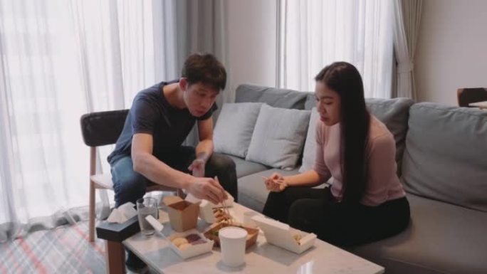 周末，一对亚洲夫妇家庭在客厅的电视前享受外卖食物