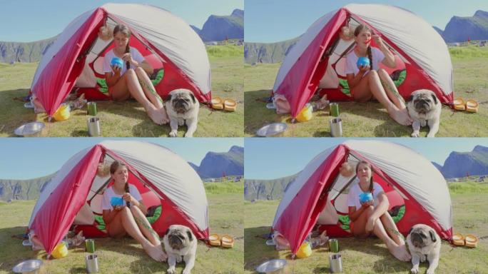 女人在罗弗滕群岛上与狗坐在帐篷里享受露营早餐