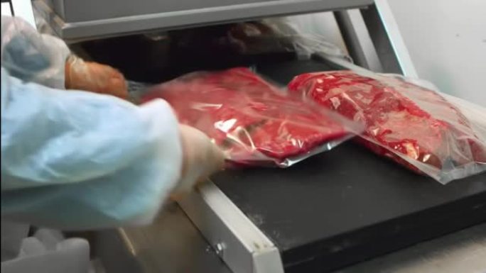 新鲜的牛肉原料装在真空玻璃纸塑料袋中。工业肉类加工厂。半成品在车间传送带上的生产线上