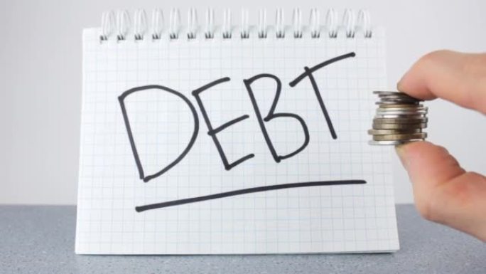 记事本和硬币上的债务这个词。债务的概念。催收，偿还债务。