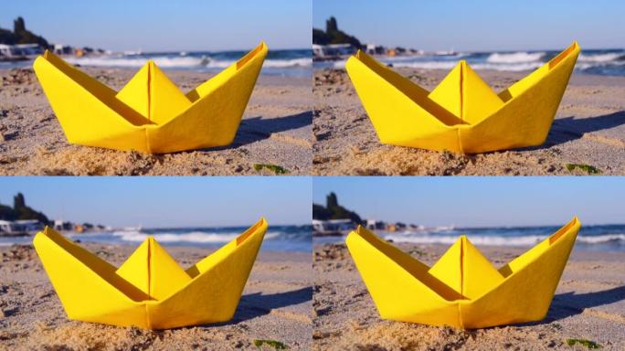 黄纸船在海边的沙滩上，在阳光明媚的日子里有白色泡沫的海浪背景下。旅游、航海、梦想、目标、决心、目的性
