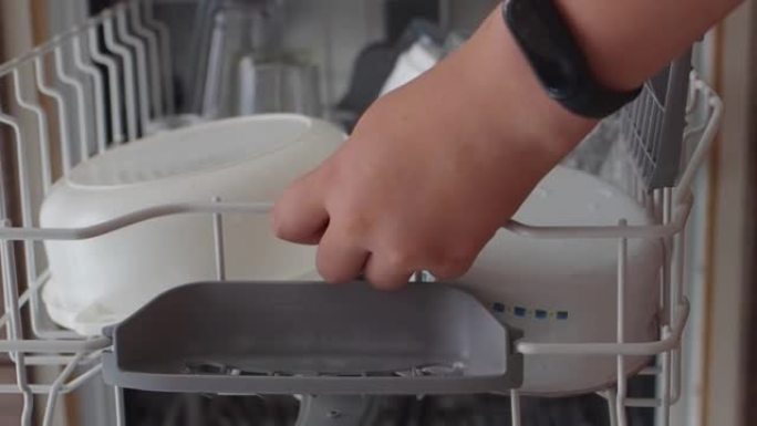 十几岁的男孩从洗碗机里拿干净的盘子。年轻人用手特写镜头卸下洗碗机。帮助妈妈。年轻人把装有脏盘子的最上