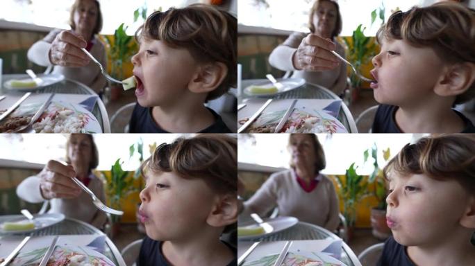 小男孩吃午饭。祖母喂养孩子孙子的食物。健康营养理念