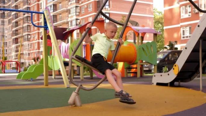 一个有趣的小男孩正在现代操场上的一个有趣的旋转木马上旋转