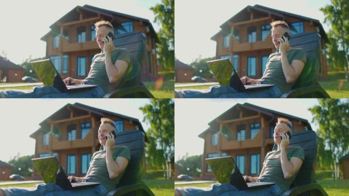 快乐的年轻人坐在乡间别墅的后院，拿着笔记本电脑打电话。慢动作