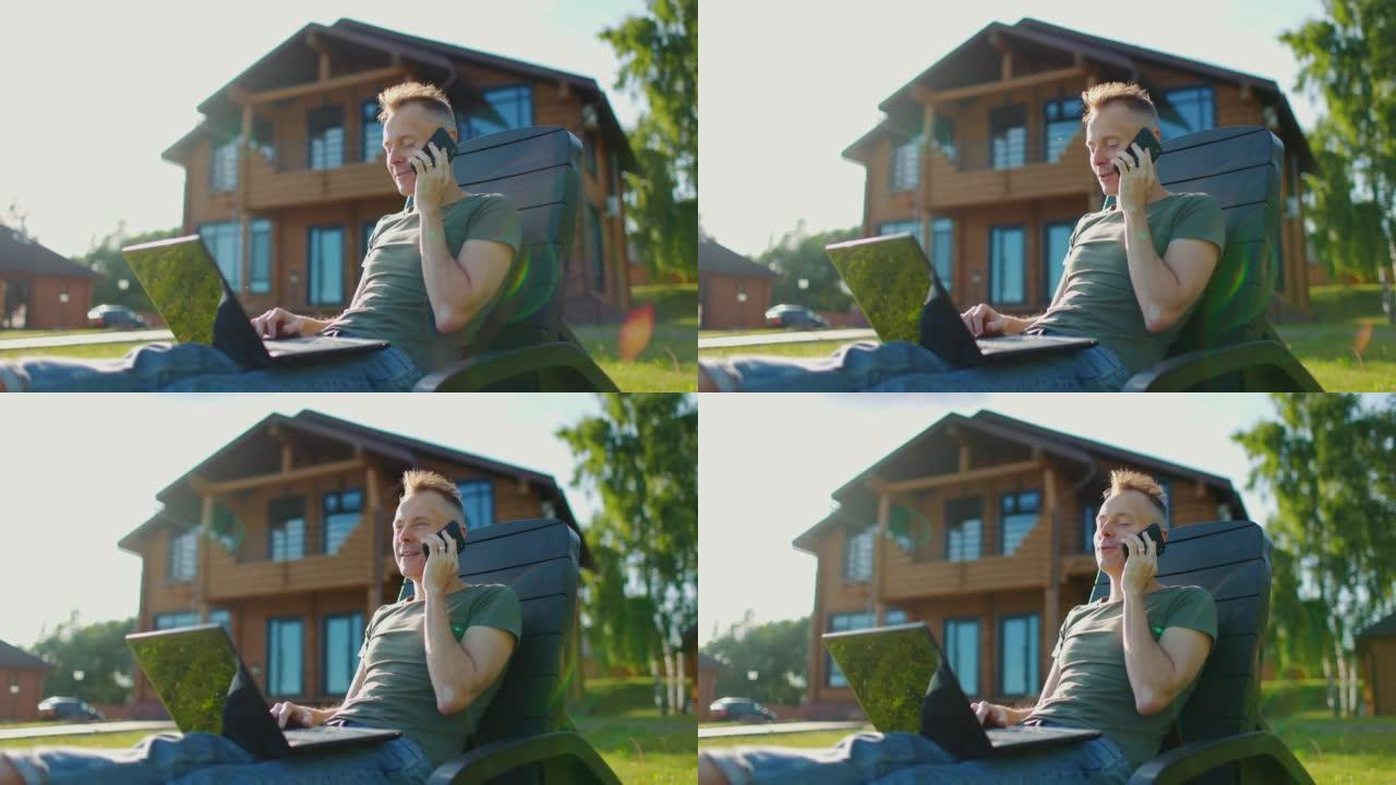快乐的年轻人坐在乡间别墅的后院，拿着笔记本电脑打电话。慢动作