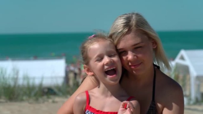 母亲和孩子看着相机，在蓝色大海的酒店海滩背景上大笑。暑假，旅游，度假。海景上的户外人