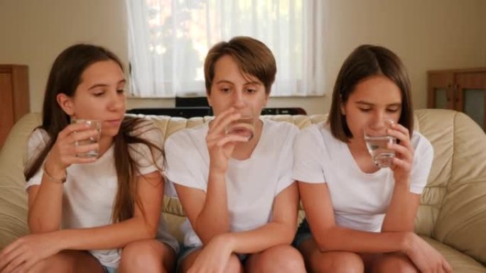 三胞胎姐妹十几岁的女孩在家看电视坐在沙发上喝眼镜上的水