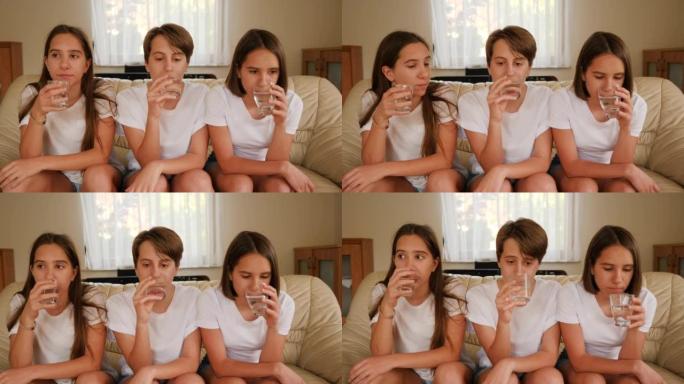三胞胎姐妹十几岁的女孩在家看电视坐在沙发上喝眼镜上的水