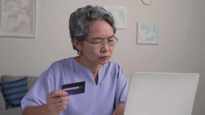 使用信用卡进行在线购物时，亚洲高级女性看起来很困惑。