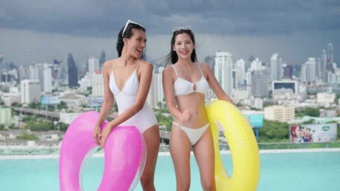 迷人而性感的年轻亚洲女性，一个穿着白色连体泳衣的女孩，而另一个穿着两件式比基尼的女孩则在游泳池边跳舞