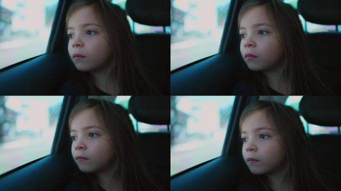 沉思的小女孩坐在汽车后座上。一个体贴的孩子特写脸望着车窗发呆