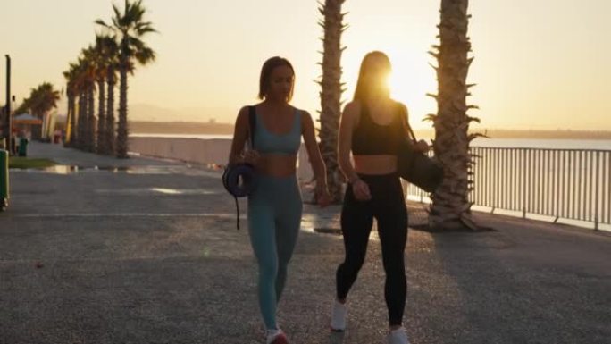 肖像两个女人穿着运动服，拿着瑜伽垫，准备户外训练，在做瑜伽之后或之前，选择锻炼的地方，去健身房，享受