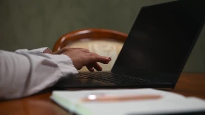 女商人的特写镜头，记者用手在笔记本电脑键盘上打字，写文本。桌子上有笔的笔记本