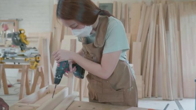 木匠在她的小型家庭作坊工作时在木板上钻了一个洞