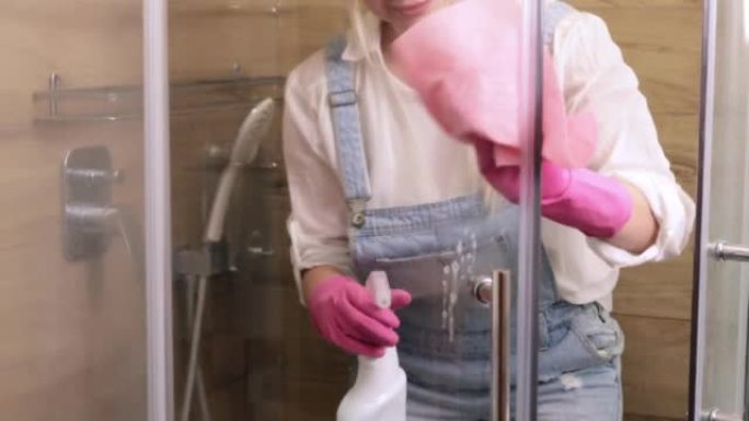 一位美丽的家庭主妇从牙菌斑上清洁淋浴房的玻璃。房屋清洁服务或女佣