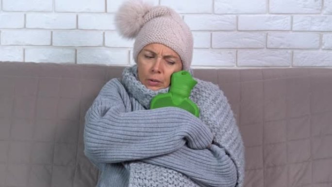 一名妇女在家中冻着加热垫和帽子，感到不适。