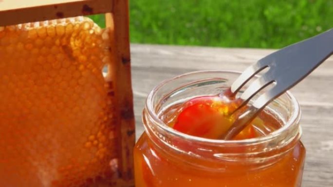 叉子上的红色草莓在玻璃罐中浸入美味的蜂蜜中