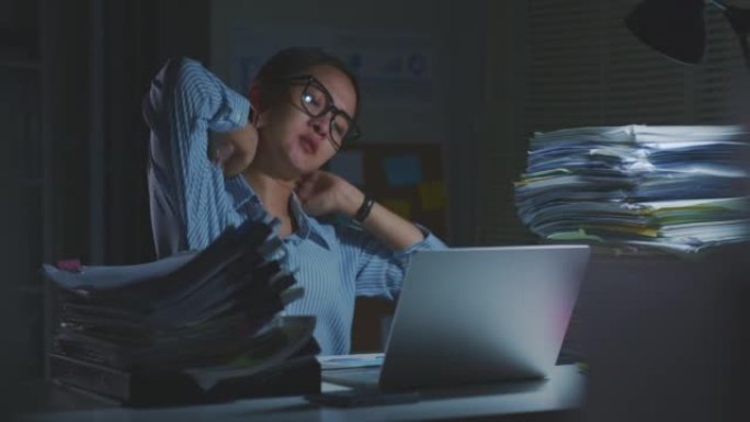疲惫的亚洲办公室员工因长时间使用笔记本电脑而感到疲倦，办公室综合症。晚上加班