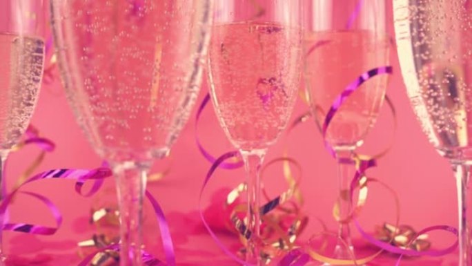 在粉红色背景的玻璃杯中起泡葡萄酒，带有五彩纸屑，呈心形和蛇形。