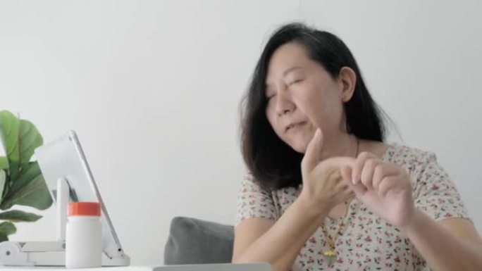 亚洲成年女性在家中通过数字平板电脑向医生打视频电话，询问自己的健康状况，这是社交疏远的生活方式概念。