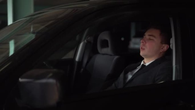一个穿着西装的结实的人在停车场的车里打哈欠，睡着了。年轻的商人累了，向后靠，睡在车里。4k
