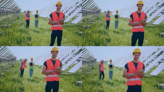 戴着安全帽的英俊生态工程师看着相机，在地面上摆姿势，他的团队分析了光伏太阳能电池板的清洁度