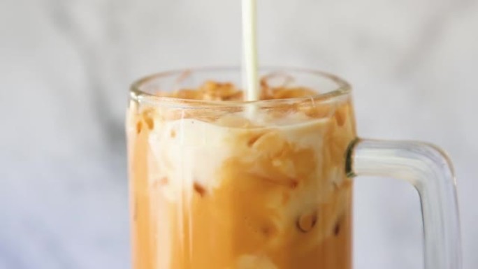 冰牛奶。泰国茶将鲜牛奶倒入玻璃杯中，一种夏季饮料概念